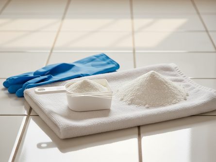 플라스틱 계량스푼과 흰색 분말 가루, 고무 장갑, 깨끗한 수건이 놓인 타일 세탁실 바닥