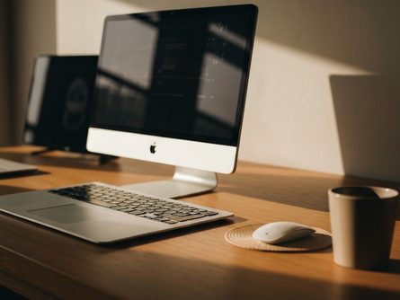 투명 플라스틱 수납함과 스텐 트레이가 나무 테이블 위에 정렬되어 있고, 옆에 채소와 과일이 놓인 주방 풍경